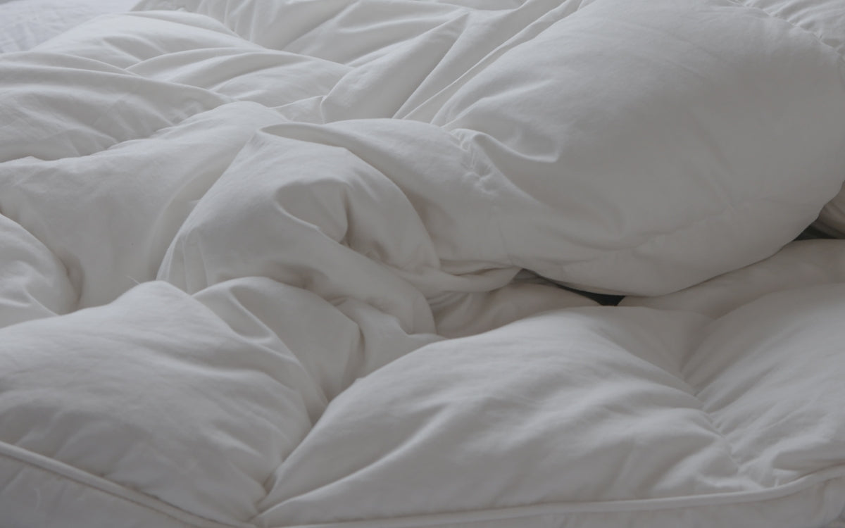 An unmade bed with white sheets and pillows