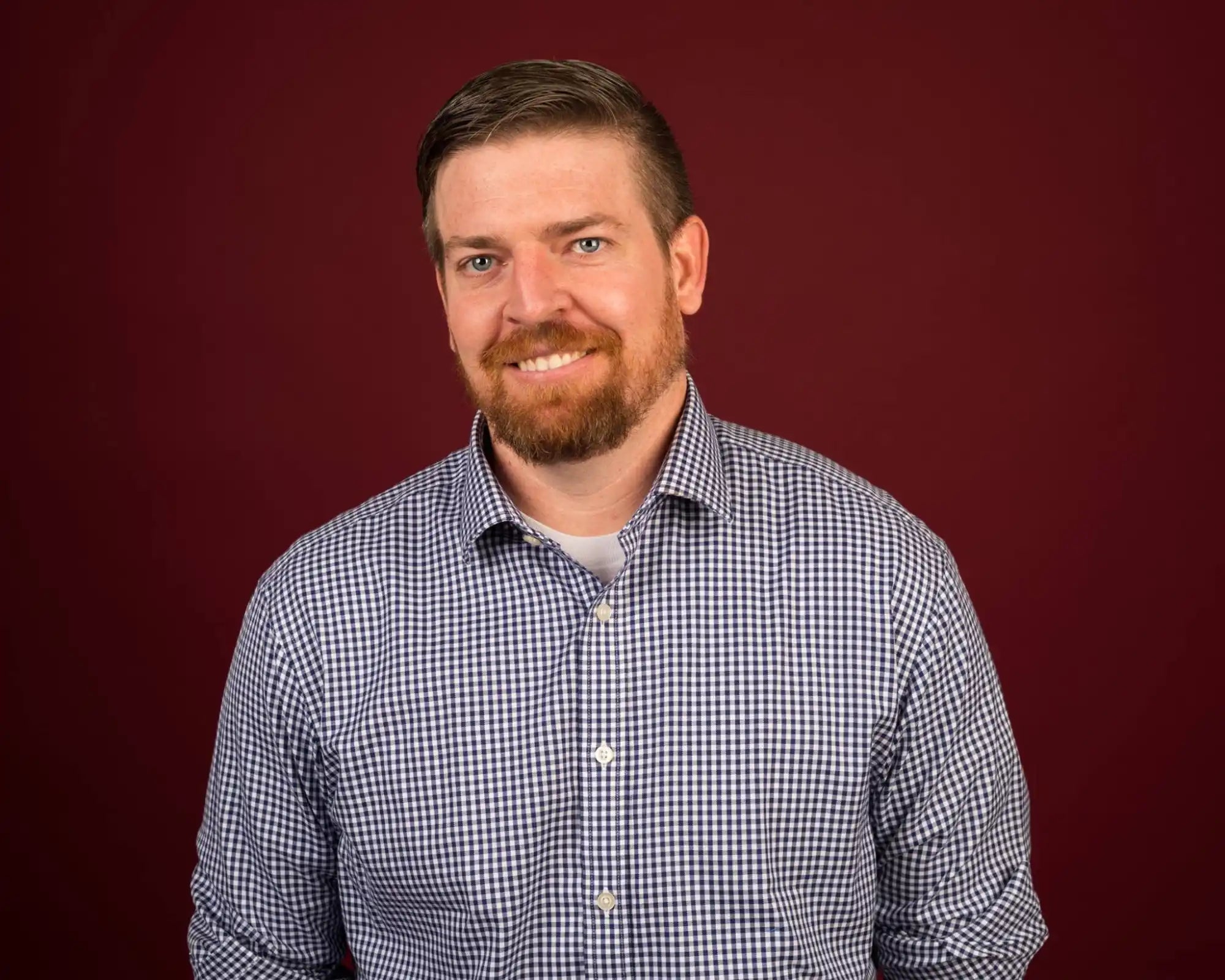 Smiling man with a beard in a checkered shirt.